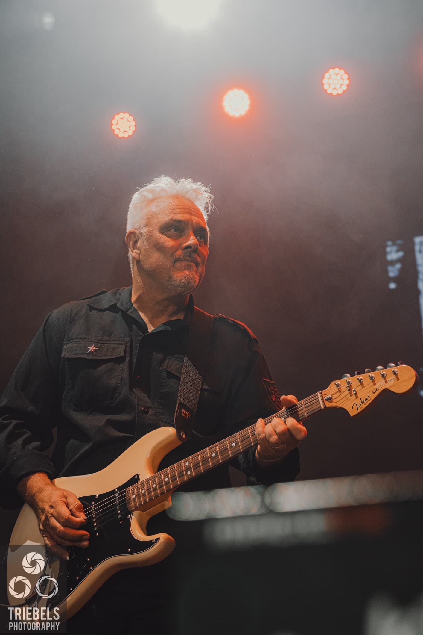 Rikki Morris on stage with Th' Dudes, playing a white Stratocaster